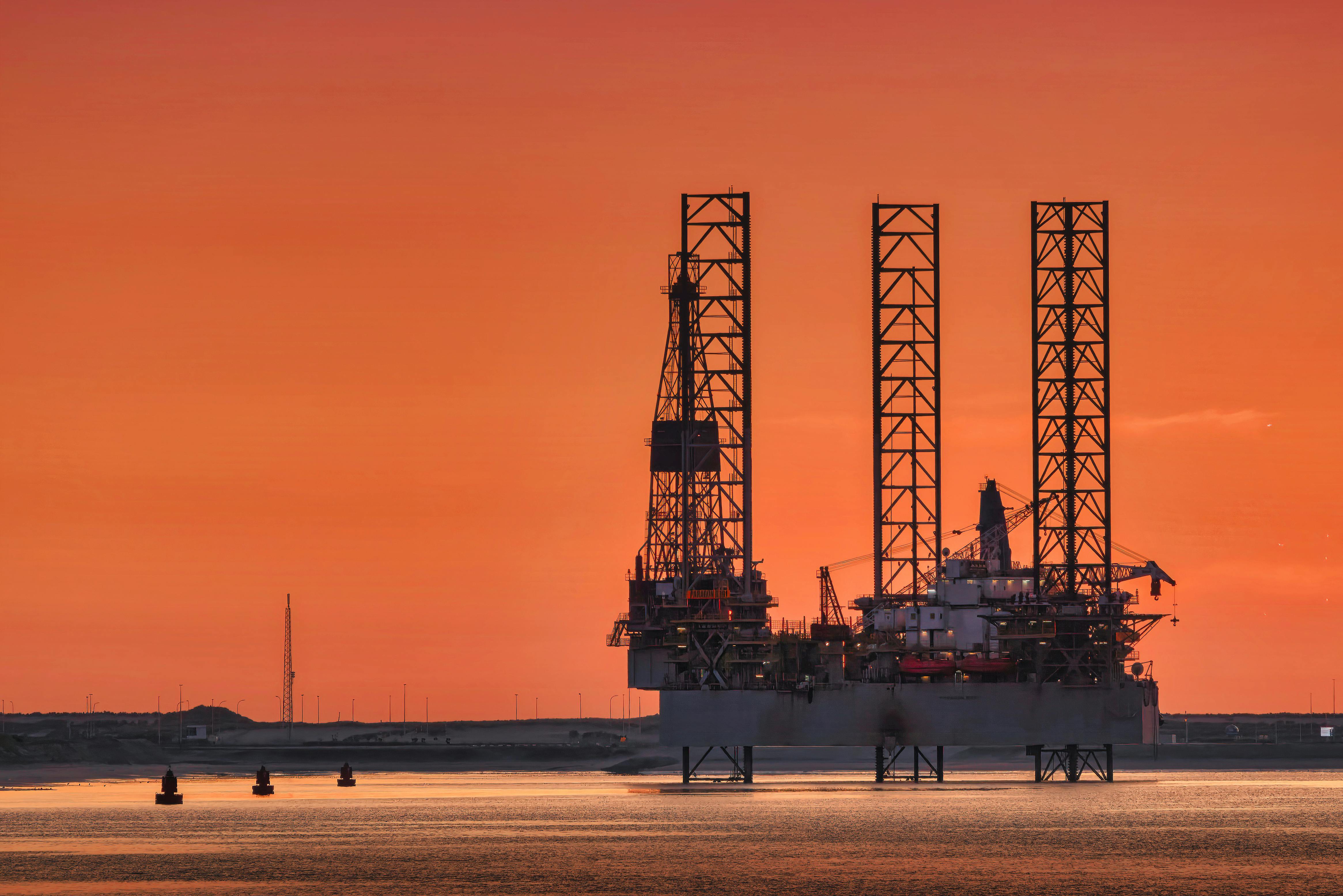 Jack-up drilling rigs silhouetted against an orange offshore sky